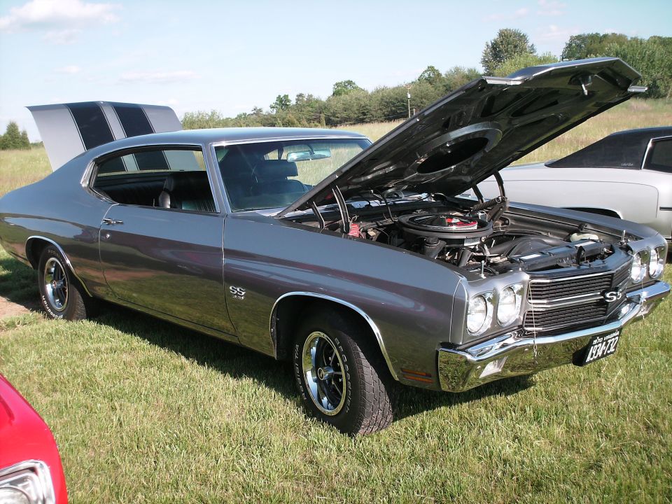 1970 Chevrolet Chevelle SS coupe, dark gray with black racing stripes, hood open, parked on grass.