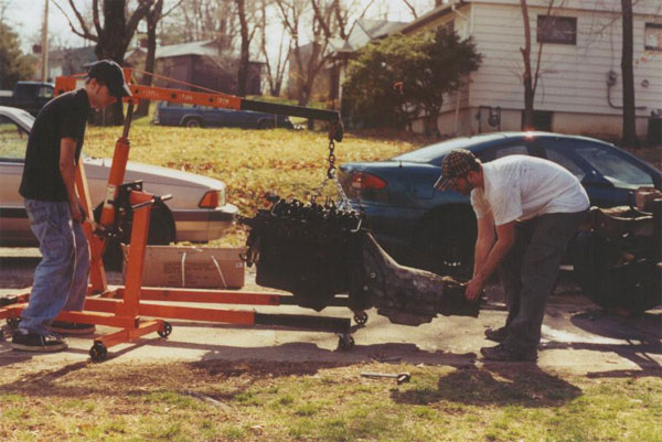 Engine being removed with an engine hoist, two cars visible
