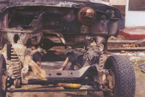1978 Ford Bronco - The front end of a vehicle is shown, heavily damaged by fire, revealing the chassis and suspension components.