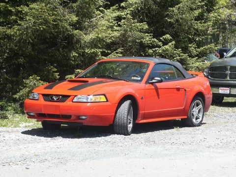 2001 Mercury Grand Marquis - Orange convertible sports car parked outdoors with trees in the background.