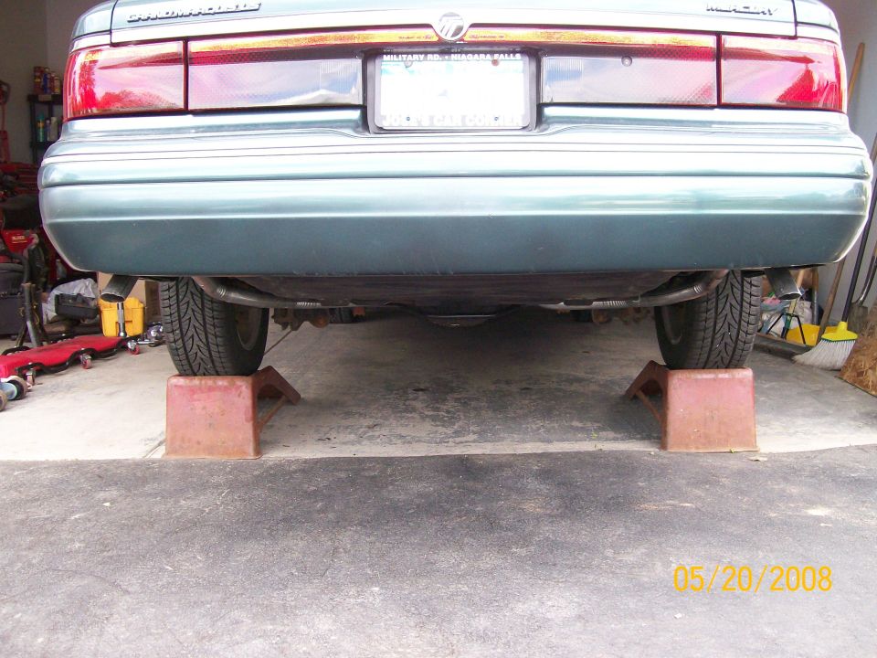 Rear view of a green sedan on car ramps in a garage.