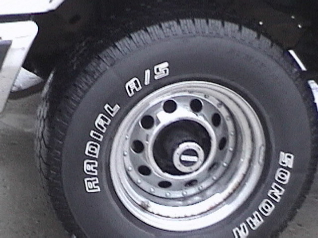 Close-up of a vehicle tire with white lettering "RADIAL M/S" and "SONORAN" on a silver rim.