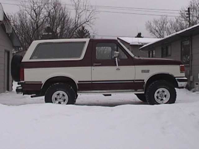 1991 Ford Bronco in maroon and white parked in snow, side view.