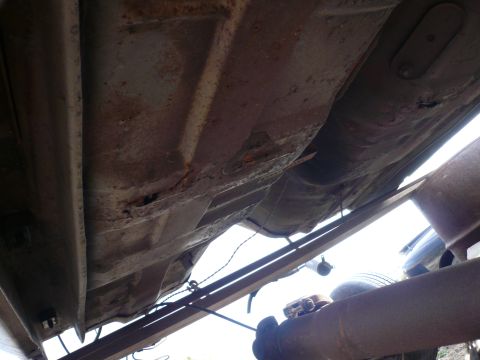 1975 Ford Ranchero - The underside of a vehicle shows significant rust and damage to the frame and floor pan. Various metal components and wiring are visible.