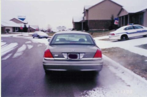 2002 Ford Crown Victoria - A gray 2002 Ford Crown Victoria is parked on a street with snow, seen from the rear.