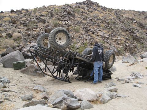 1994 Jeep YJ - A custom-built off-road buggy has rolled over in a rocky, desert environment, with a person observing the scene.