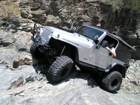 1986 Toyota Hilux - A silver Jeep Wrangler Rubicon navigates a rocky trail, demonstrating its off-road capabilities.