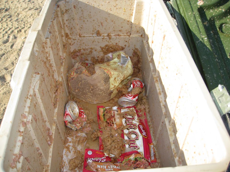 Open cooler filled with food scraps, crushed cans, and packaging. A green object is visible to the right