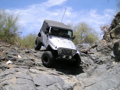 1986 Toyota Hilux - A silver Jeep Wrangler navigates a rocky off-road trail under a blue sky.