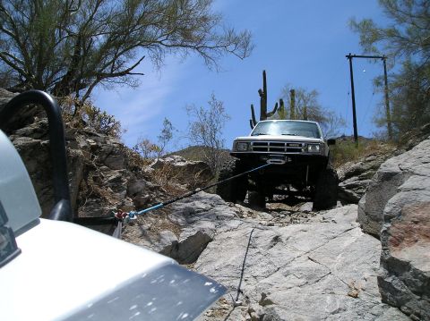 1986 Toyota Hilux - A white 1986 Toyota Hilux navigates a steep, rocky trail, assisted by a winch.