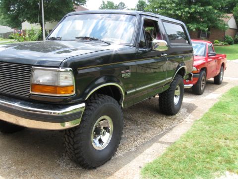 1994 Ford Bronco - A black 1994 Ford Bronco is parked on a gravel driveway next to a red pickup truck.