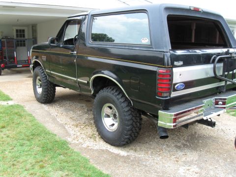 1994 Ford Bronco - This black 1994 Ford Bronco features chrome accents and large off-road tires, viewed from the rear three-quarter angle.