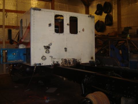 1992 Ford Bronco - A white truck cab is mounted on a black chassis, undergoing modifications in a workshop environment.