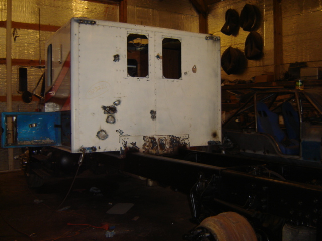 White truck cab with two window openings on a black chassis, in a workshop