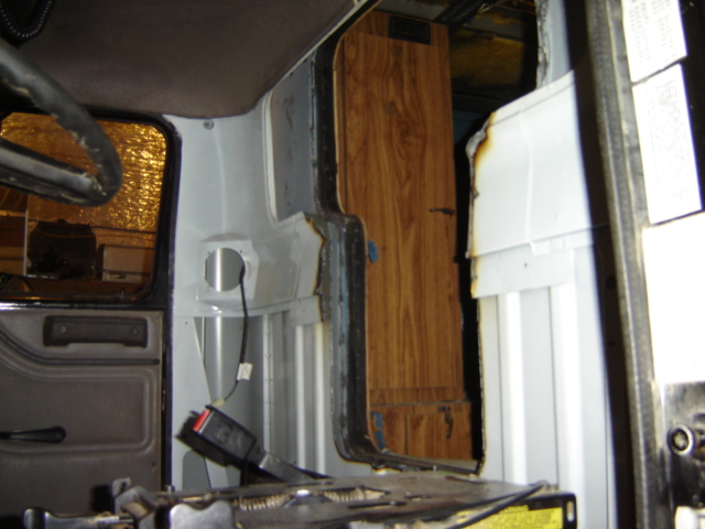 Interior view of a vehicle showing disassembled door panel, seatbelt, and wood-paneled section