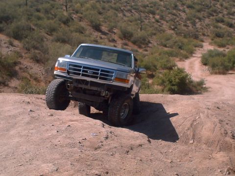 1991 Ford Bronco - Silver Ford Bronco with lifted suspension driving on a dirt trail in a desert landscape.