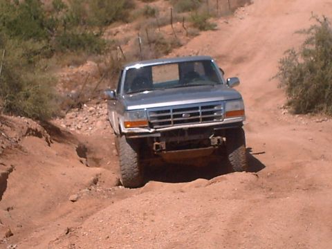 1991 Ford Bronco - A silver Ford F-150 navigates a rough dirt road, its front bumper showing signs of damage.