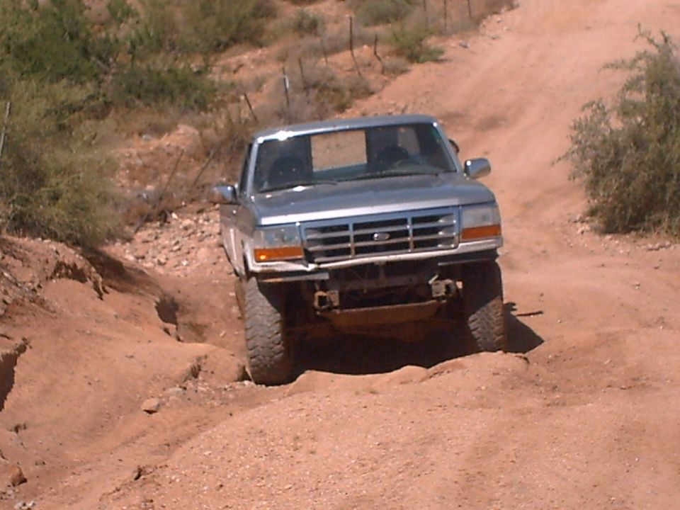 Silver Ford F-150 truck with a damaged front bumper driving on a dirt path
