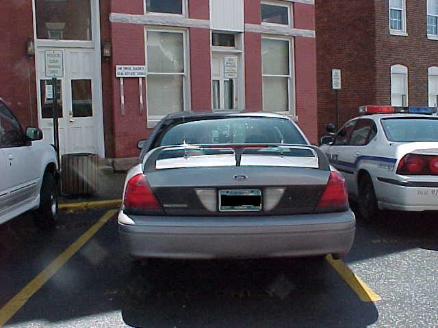 Rear of gray Ford Crown Victoria sedan parked next to a police car