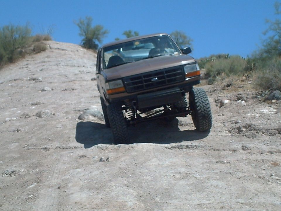 Brown Ford Bronco with lifted suspension driving on a dirt hill