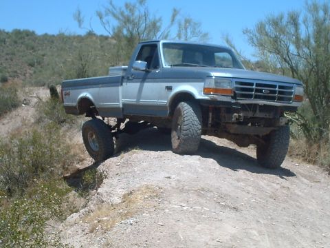 1991 Ford Bronco - This lifted pickup truck, likely a 1992 model based on its grille, navigates a dirt path in a dry, arid landscape.