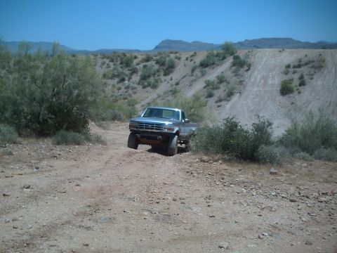 1991 Ford Bronco - A silver pickup truck navigates a dusty, off-road trail under a clear blue sky.