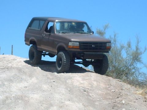 1991 Ford Bronco - This 1991 Ford Bronco is captured mid-climb on a dusty, off-road trail under a clear blue sky.