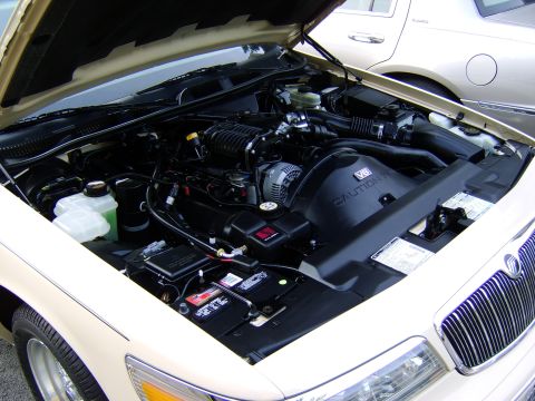 1996 Mercury Grand Marquis - Engine bay of a 1996 Mercury Grand Marquis, showing the V8 engine and supercharger. A second vehicle is visible in the background.
