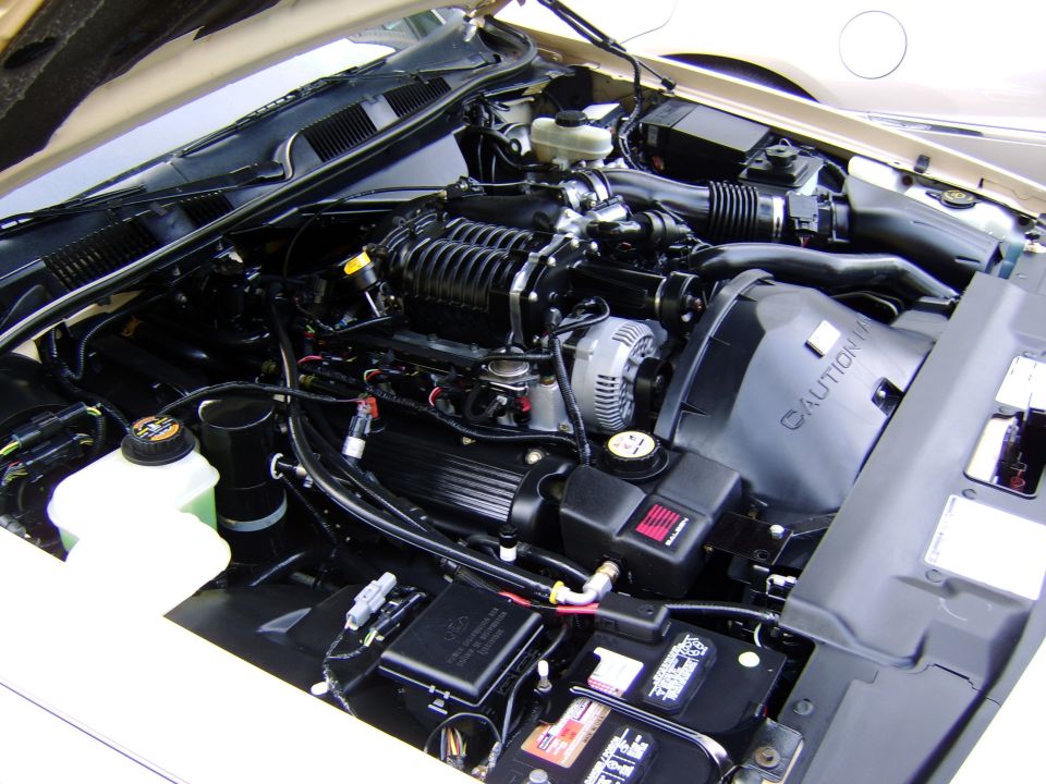 Engine bay with supercharger, black intake tube, and battery visible