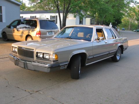 1988 Mercury Grand Marquis - A tan 1988 Mercury Grand Marquis sedan is parked in a driveway next to a tan minivan.
