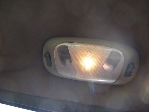 1989 Ford Bronco - Close-up of an oval overhead dome light lit up against a gray headliner, with two dark rocker-style map light switches flanking the frosted…