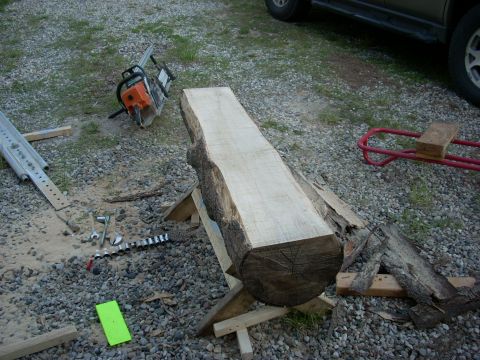 2000 Chevrolet Tahoe - A chainsaw and a large log are set up on sawhorses, with various tools nearby on a gravel surface.