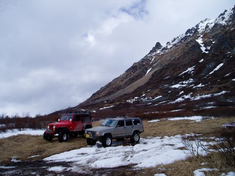 2000 Ford E350 - Two Jeeps are parked on a snowy mountain slope with sparse vegetation under a cloudy sky.