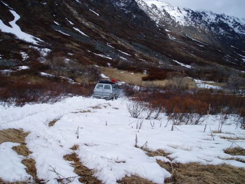 2000 Ford E350 - A van navigates a snowy path on a mountain, with a rocky slope in the background.