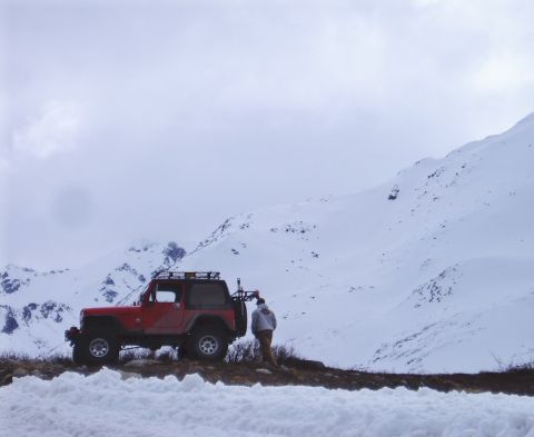 2000 Ford E350 - A red Jeep Wrangler is parked on a snowy mountain road with a person standing beside it.