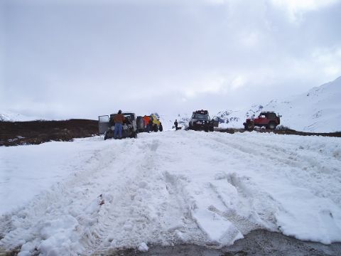 2000 Ford E350 - A group of off-road vehicles are stopped in a snowy mountain area, with people attending to them.