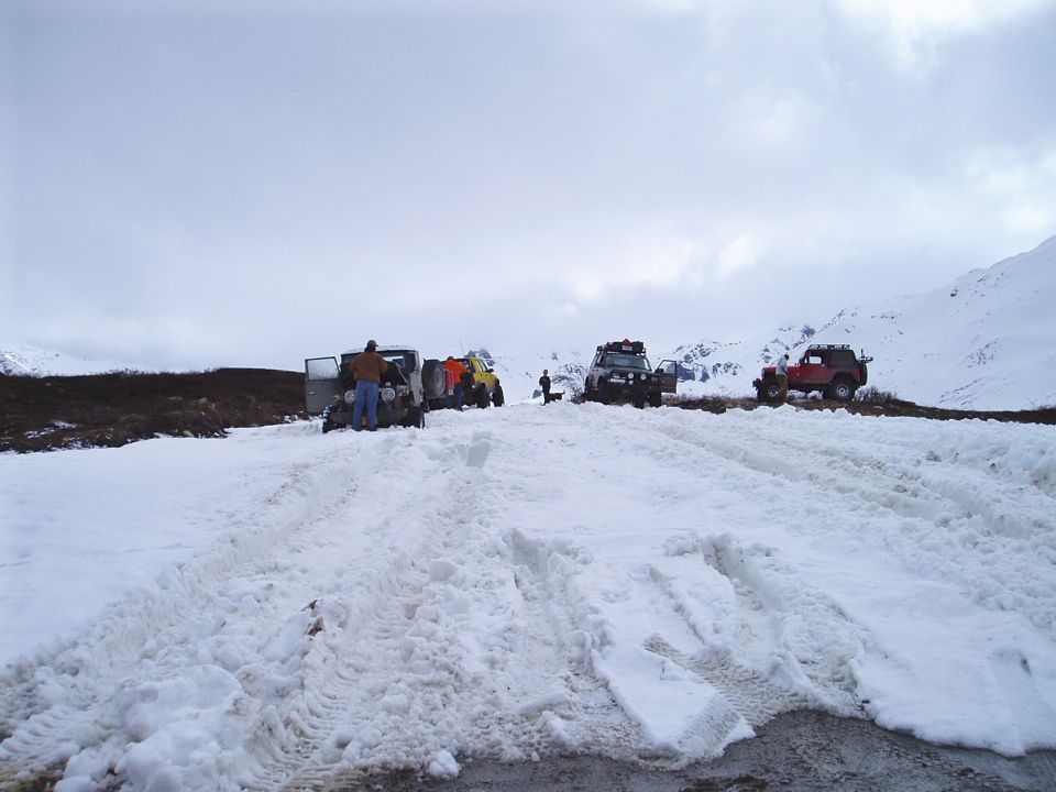Several off-road vehicles parked in a snowy mountain pass with people around them