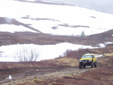 2000 Ford E350 - A yellow SUV navigates a muddy, off-road path in a snowy, mountainous landscape.