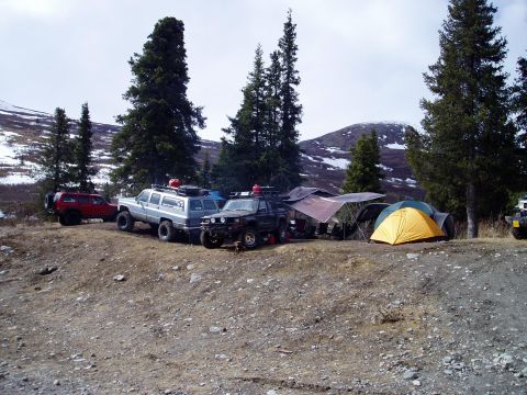 2000 Ford E350 - Several off-road vehicles are parked at a campsite with tents and trees in a mountainous landscape.