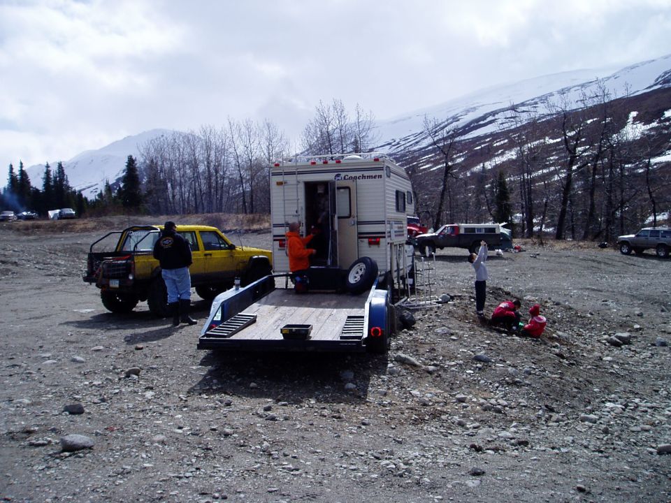 Yellow Jeep Cherokee towing an empty trailer with a Coachmen camper attached. Mountains in background