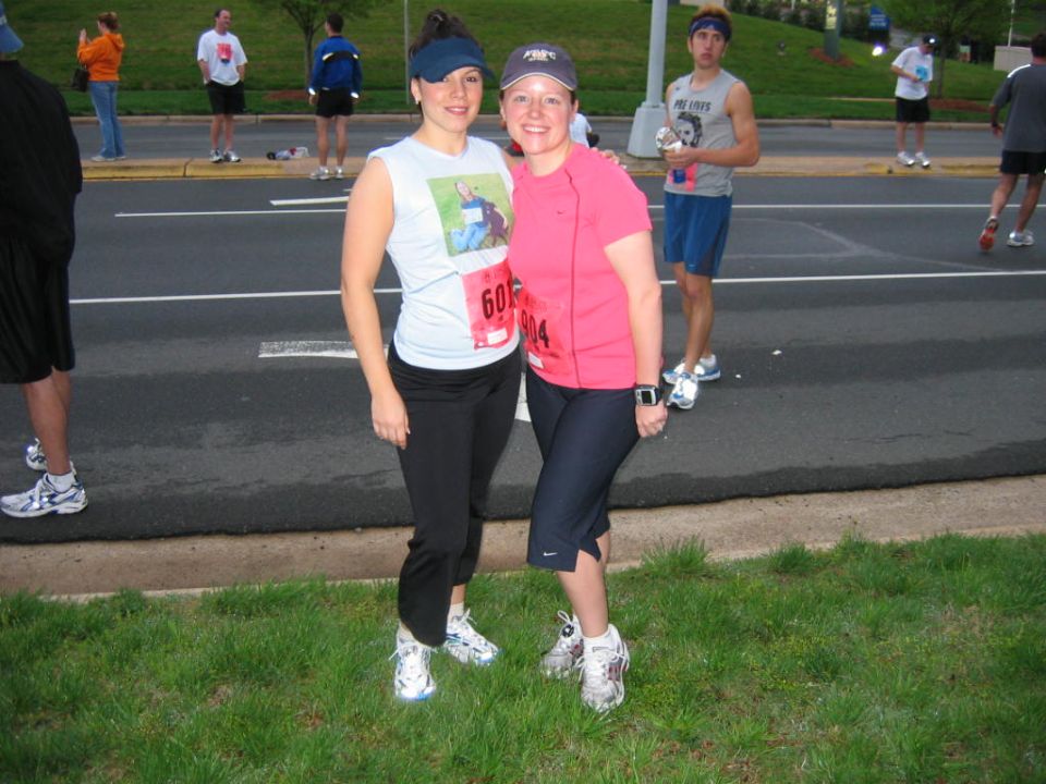 Two women in running gear pose for a photo at a race, wearing bib numbers
