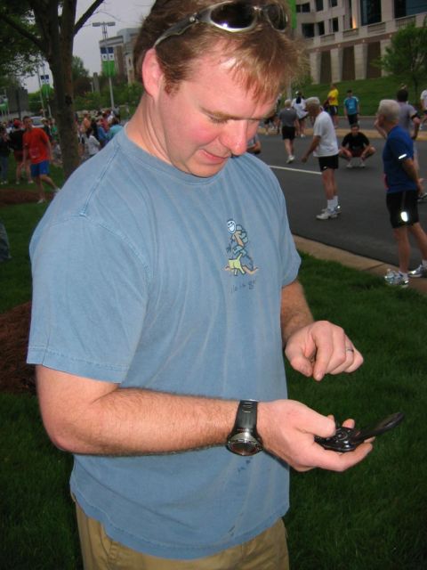1985 Ford LTD Crown Victoria - A man checks his phone while participants in a race gather behind him.