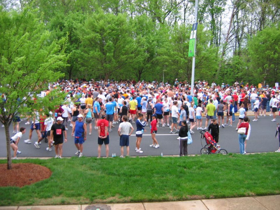 Large group of people gathered for a marathon, with trees and a banner pole in the background