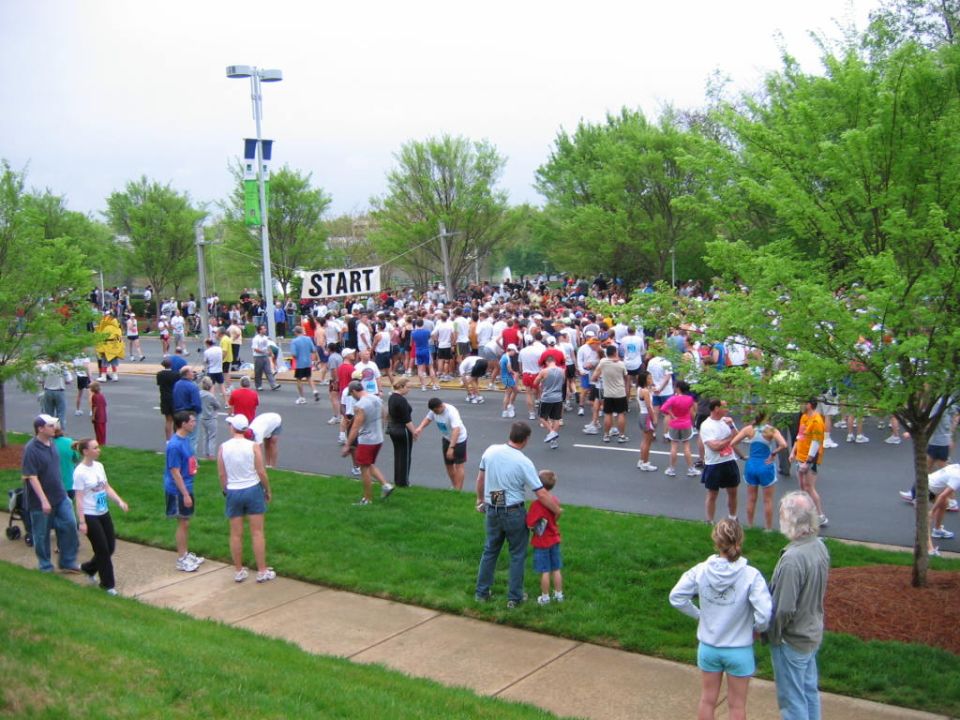 Crowd gathered at a marathon start line with a banner that says START. People are standing on the road and grass
