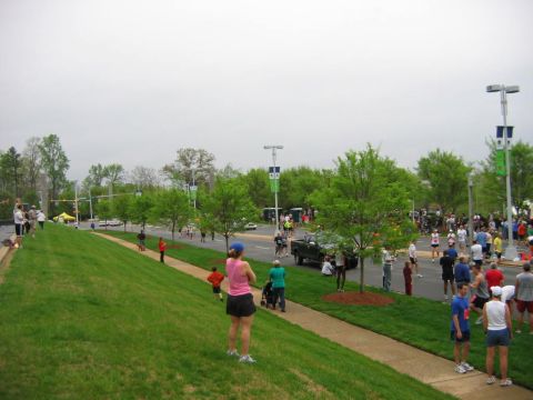 1985 Ford LTD Crown Victoria - Spectators observe a marathon event with runners and support staff along a street.