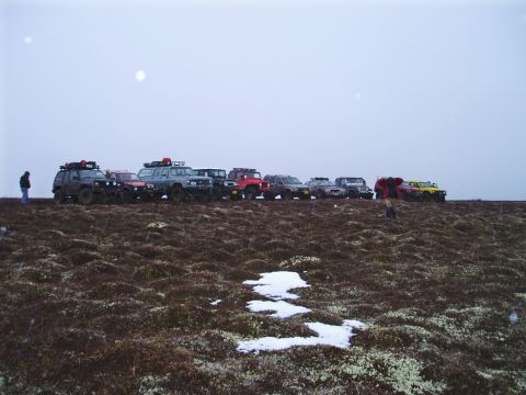 2000 Ford E350 - A group of off-road vehicles are parked on a hill with patches of snow and moss.