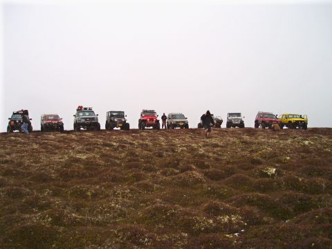 2000 Ford E350 - Multiple off-road vehicles are lined up on a hill, with people standing near them.