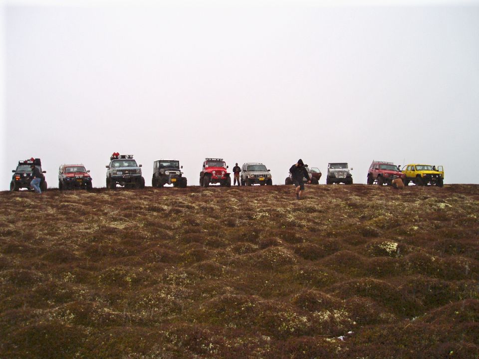 Line of SUVs and Jeeps parked on a hill with brown, mossy ground under a hazy sky