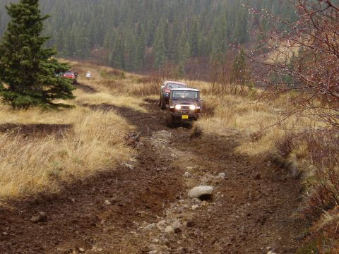 2000 Ford E350 - Off-road vehicles tackle a challenging muddy trail in a wooded, hilly area.
