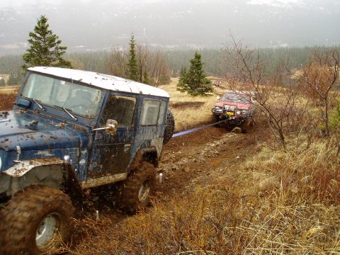 2000 Ford E350 - Two off-road vehicles are stuck in the mud, with one towing the other.